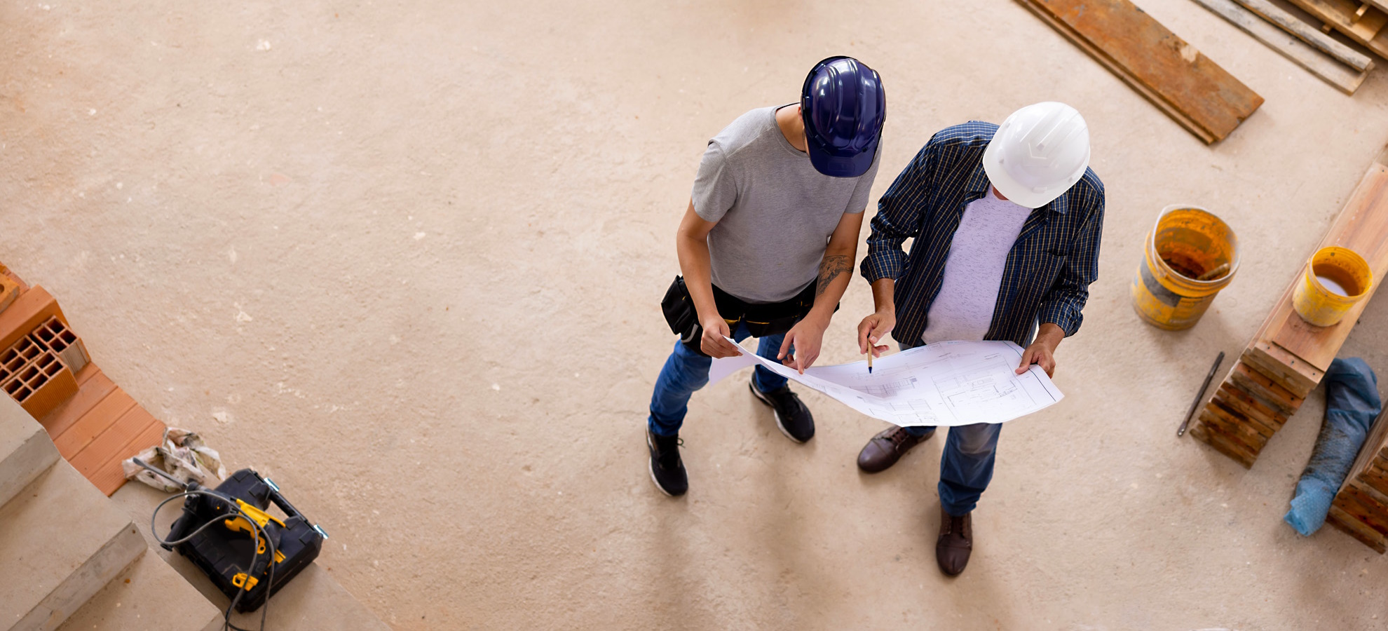 Zwei Männer mit Helm und Konstruktionszeichnung auf Baustelle